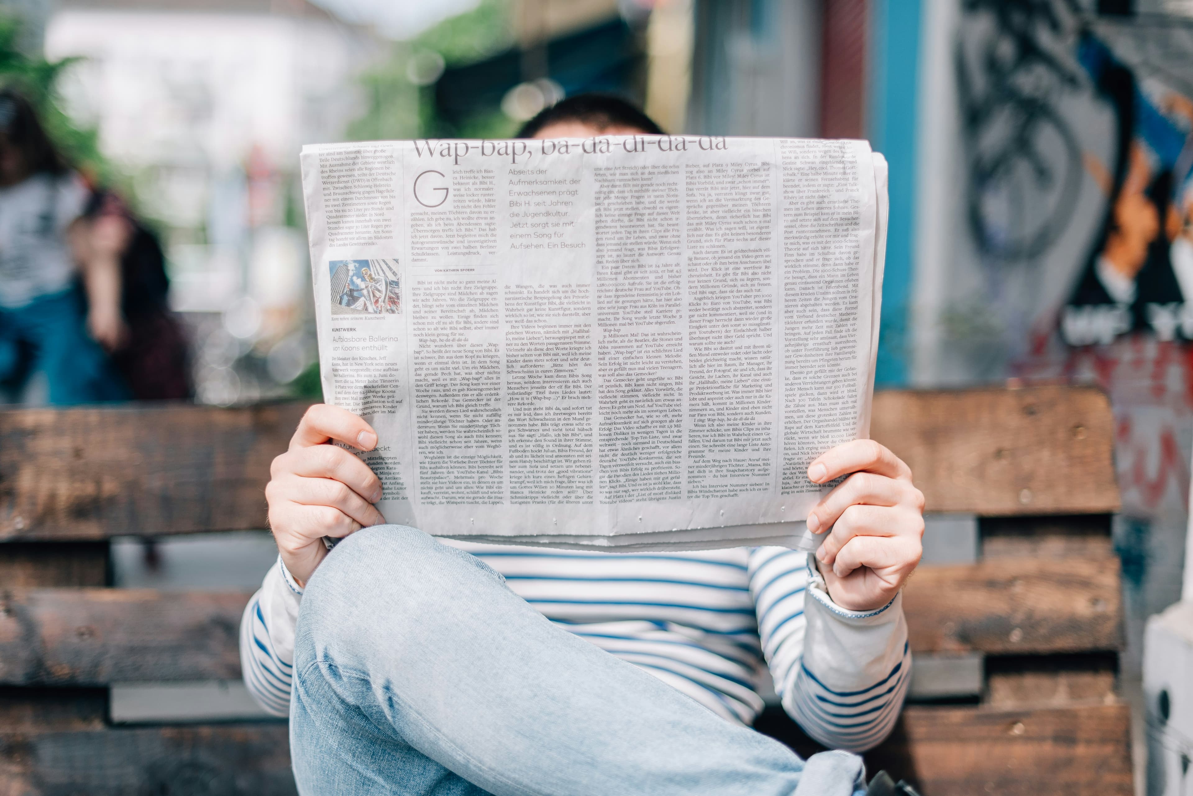 Mann lieest seine Zeitung auf einer Parkbank